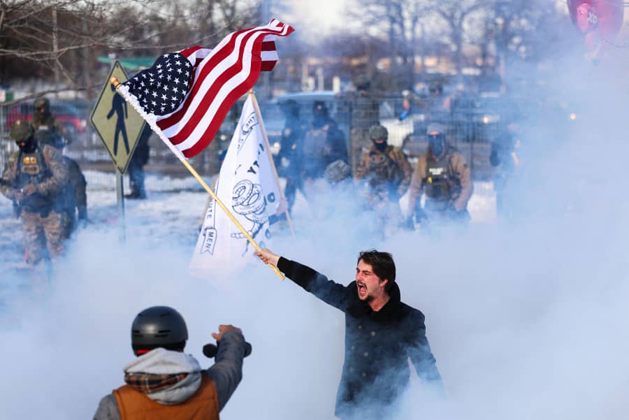 A counter-protester waves a U.S. flag next to protesters near the Bishop Henry Whipple Federal Building in Minneapolis on Jan. 9, 2026. 