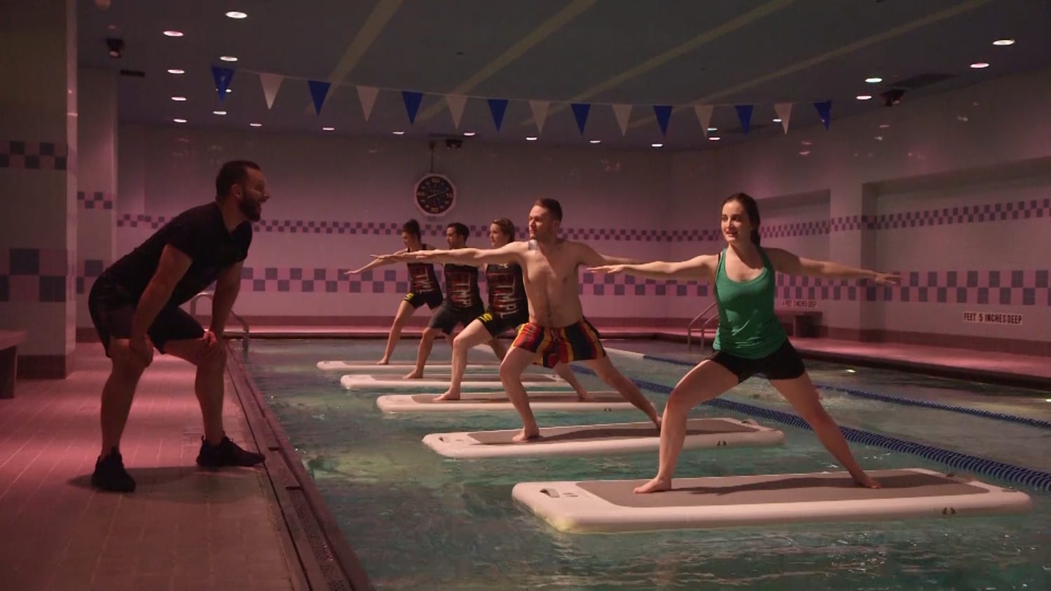 Aqua yoga class at TMPL Gym with participants balancing on floating mats in the pool.