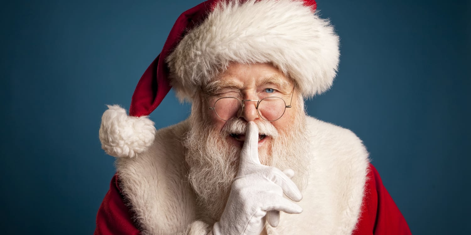 A performer dressed as Santa Claus sits behind a Plexiglas barrier