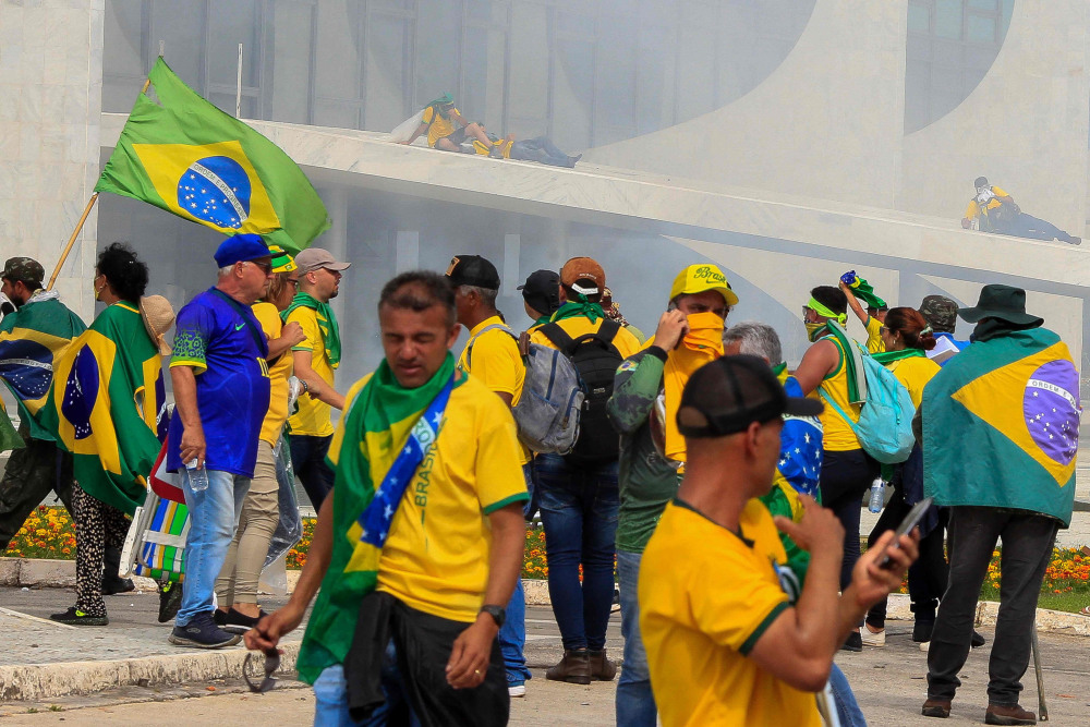Apoiadores do ex-presidente brasileiro Jair Bolsonaro ao invadir o Palácio do Planalto são atingidos por gás lacrimogêneo disparado pelas forças de segurança, em Brasília, em 8 de janeiro de 2023.