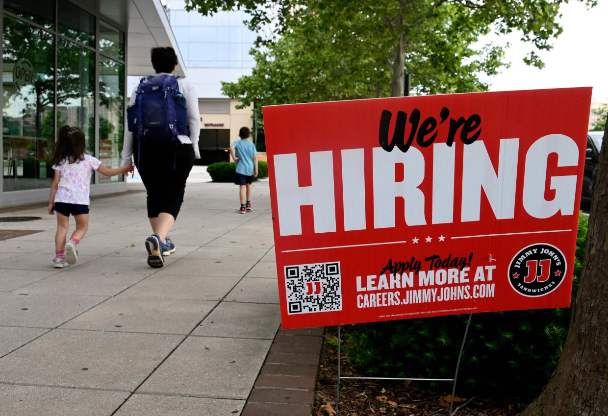 People walk past a "now hiring" sign outside a restaurant in Arlington, Va., on June 3, 2022.