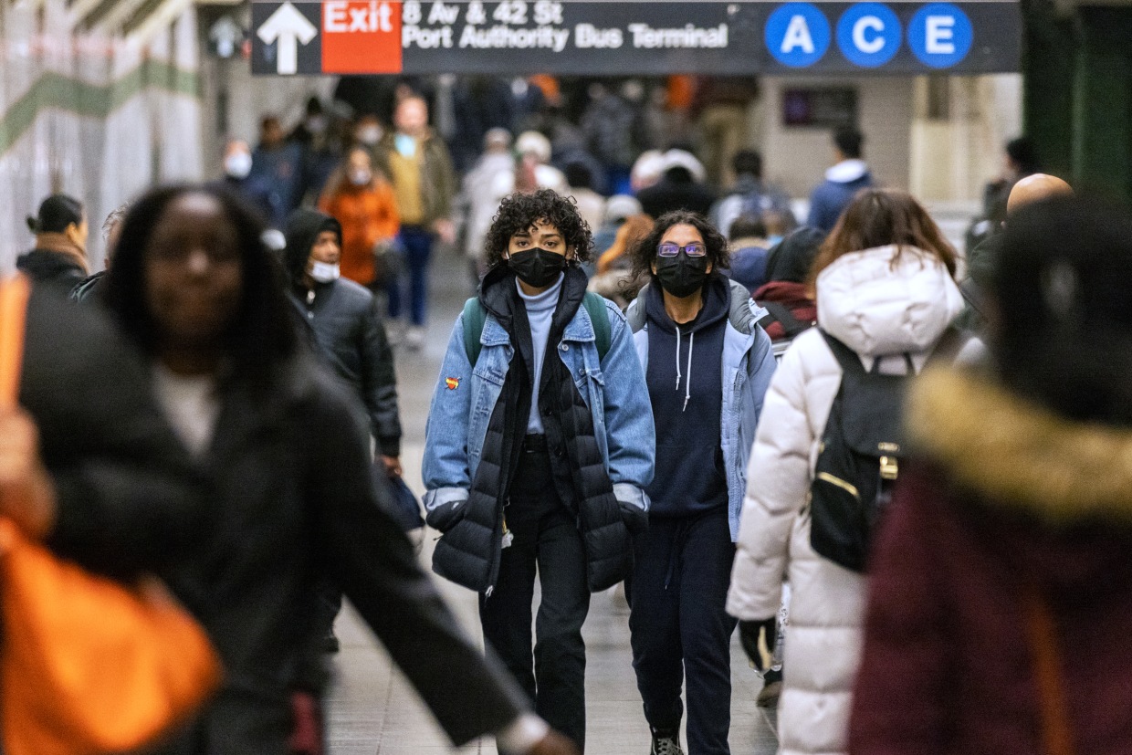 Two people wearing masks walk among commuters in a subway station in New York