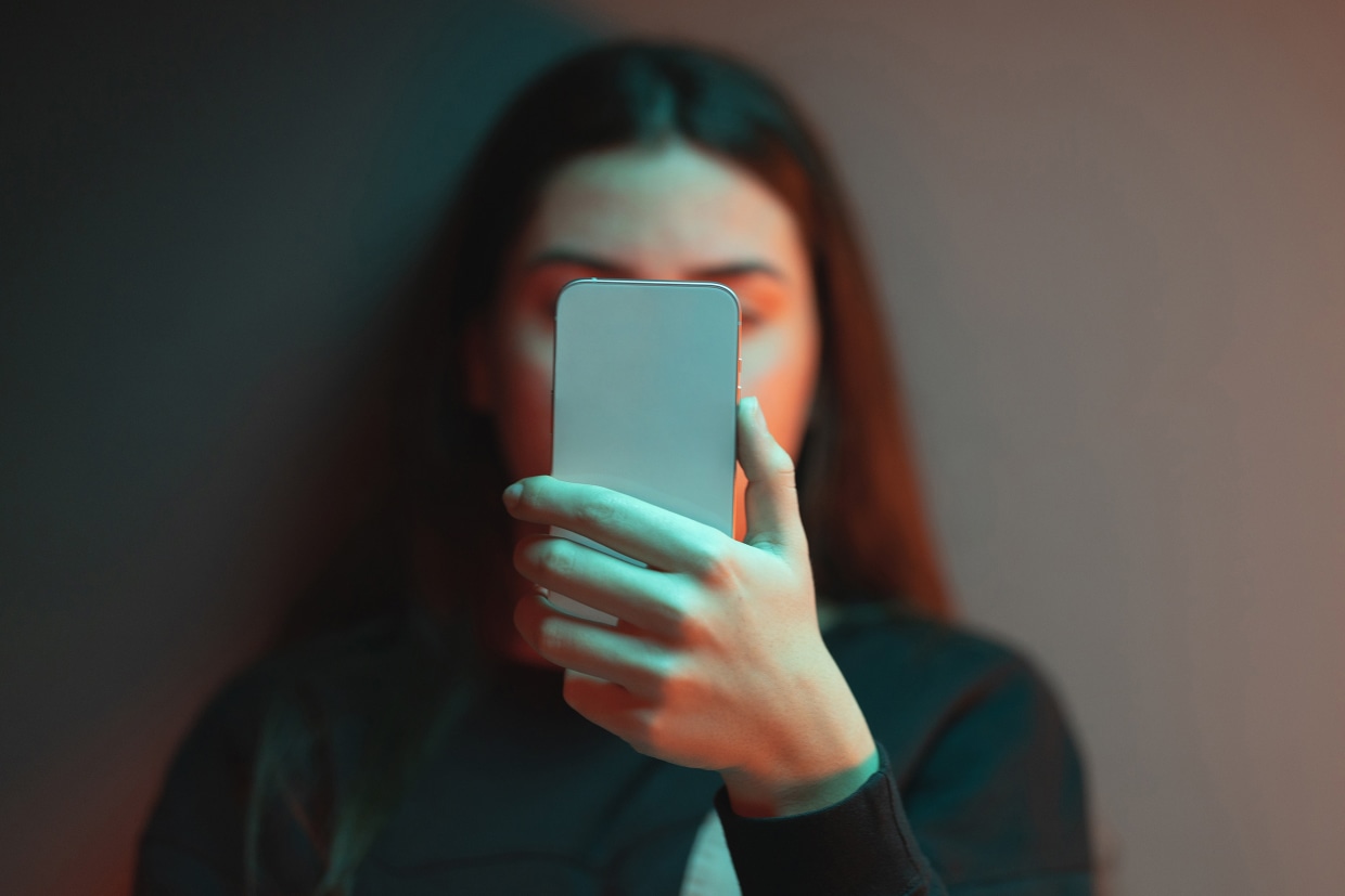 Photo of young person facing camera and staring at cell phone partially blocking their face