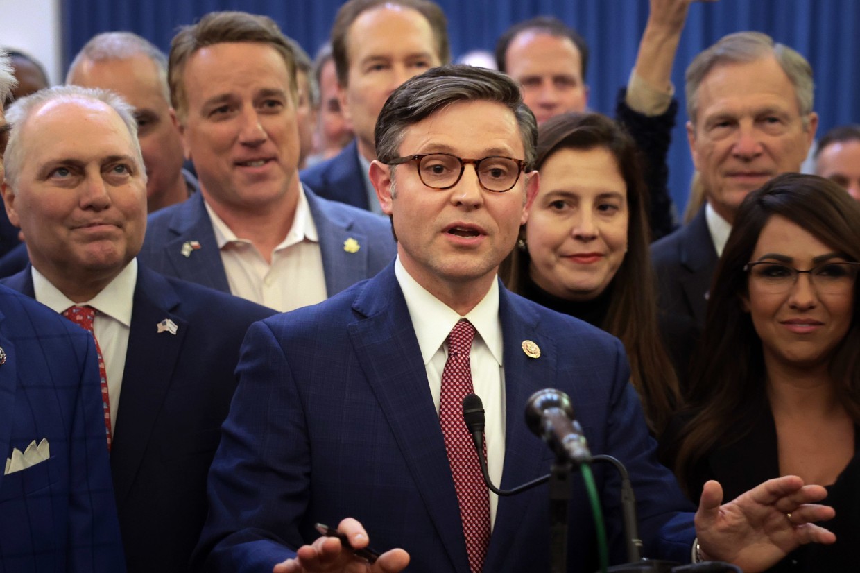 House Speaker Mike Johnson talks at a podium surrounded by House Republicans