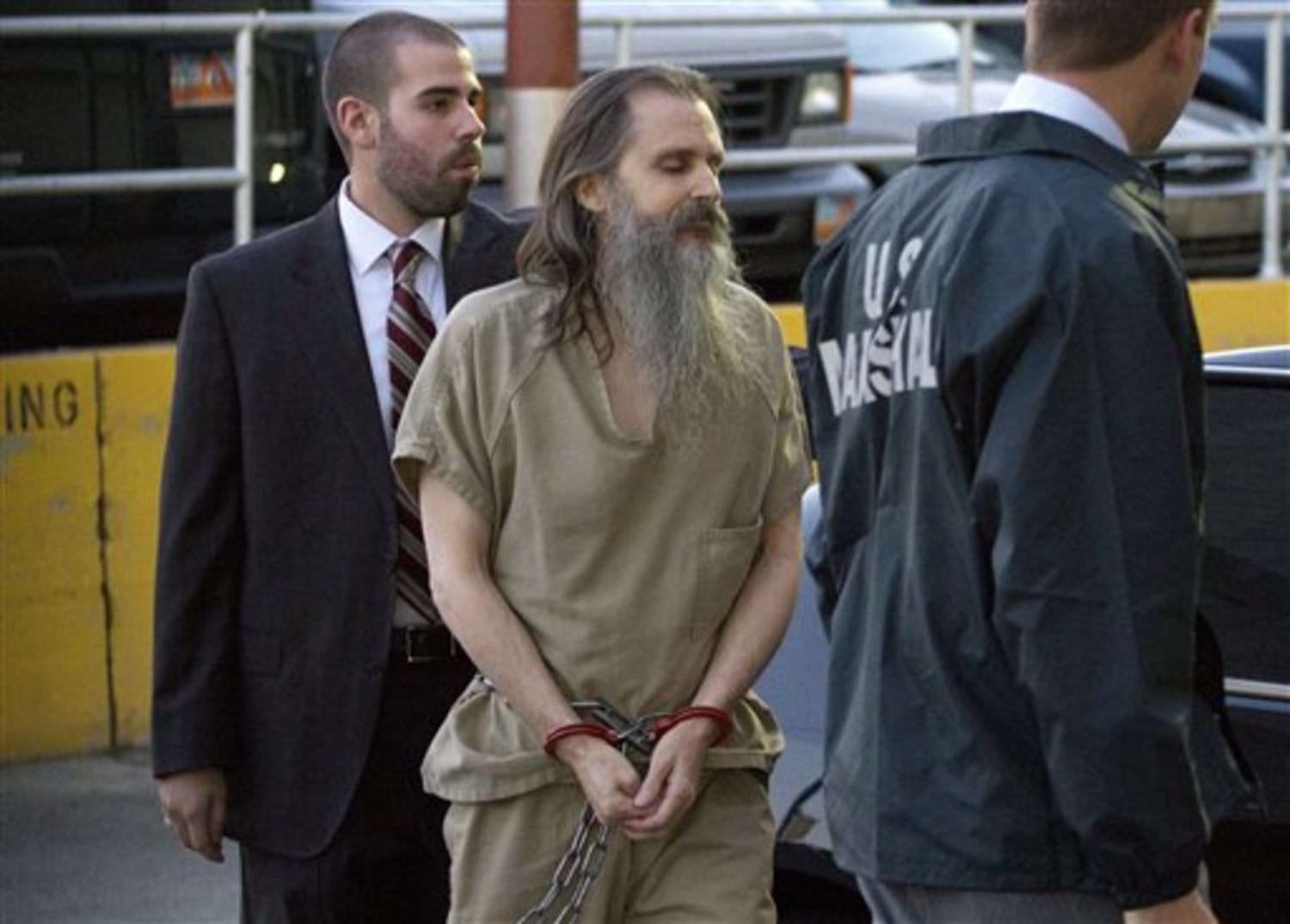 Brian David Mitchell is escorted in handcuffs by U.S. Marshals while wearing a prison uniform.