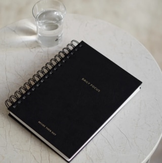 Inside Then Out Daily Focus Planner on a marble table next to a glass of water.