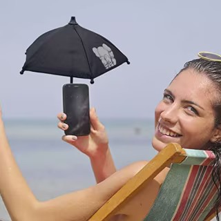 Woman at the beach, using her phone with a tiny umbrella over it