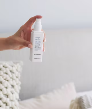 Hand spraying the Deep Sleep Pillow Spray on a pillow on a bed