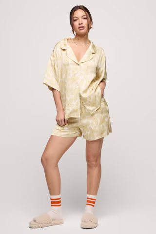 Photo of woman taking a mirror selfie in yellow, floral print pajamas in her bedroom.