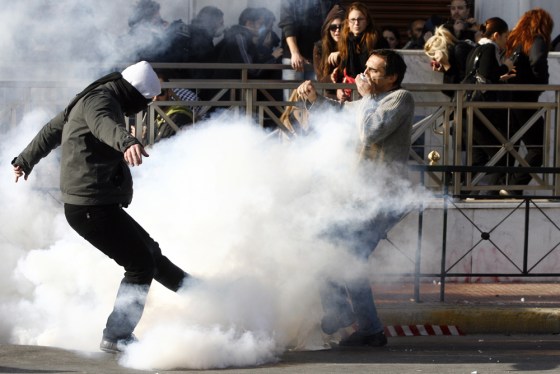 Image: A Greek youth kicks a tear gas away during clashes with riot police