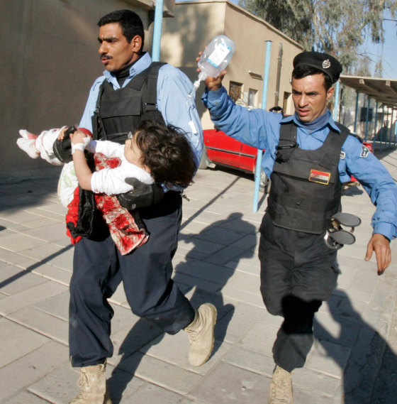 Image: Iraqi policemen rush a child wounded in a bomb attack into a hospital