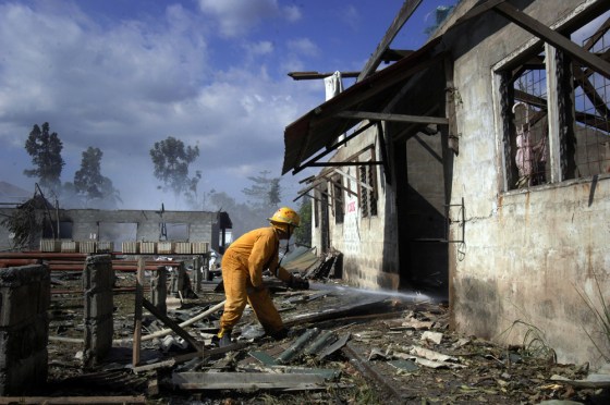 Image: A firefighter trains his hose inside a building filled with unexploded firecrackers of a factory