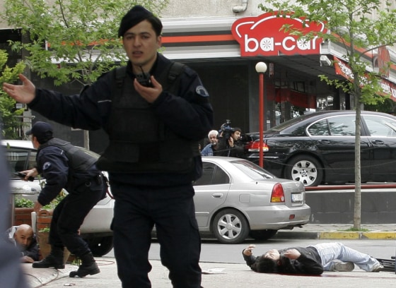 Image: A man takes cover, left, as a wounded man lies motionless