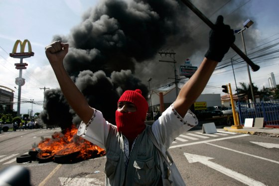 Image: A supporter of Honduras' President Zelaya demonstrates in front of burning tires outside the presidential residency in Tegucigalpa