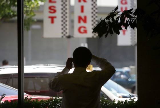 Image: A man talks on a cell phone as he looks at new cars through a window