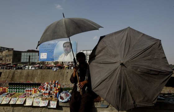 Image: A roadside vendor protects himself from the sun as he sells his wares in front of a portrait of main presidential challenger Abdullah Abdullah in Kabul