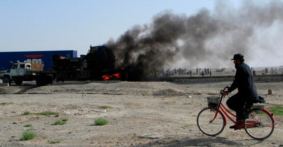 Image: A man rides his bicycle past burning vehicles along the Chaman Pakistan-Afghanistan border