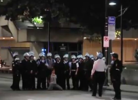 A video posted on YouTube apparently shows about 15 police officers in riot gear posing for a photo with a man they detained kneeling in front of them.