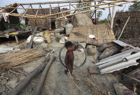 Image: A boy holds a bicycle tyre in front of damaged huts in the cyclone-hit area of Asuragar village