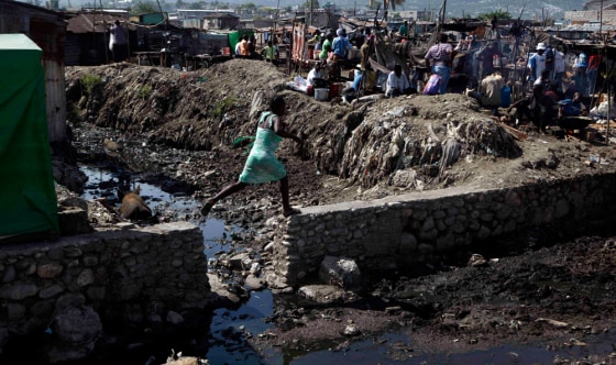 Image: A woman jumps along a wall near La Saline market in Port-au-Prince