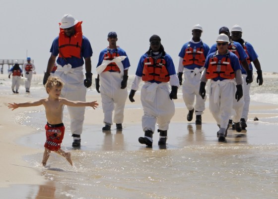 Image: Boy plays in surf as oil clean up crew combs beach