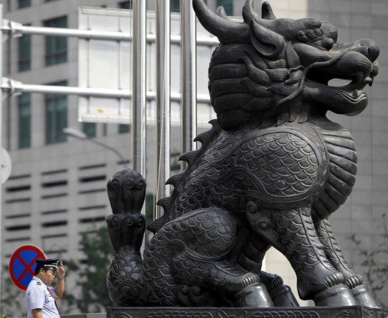 Image: A security guard adjusts his cap behind a Qilin sculpture at Beijing's Financial Street
