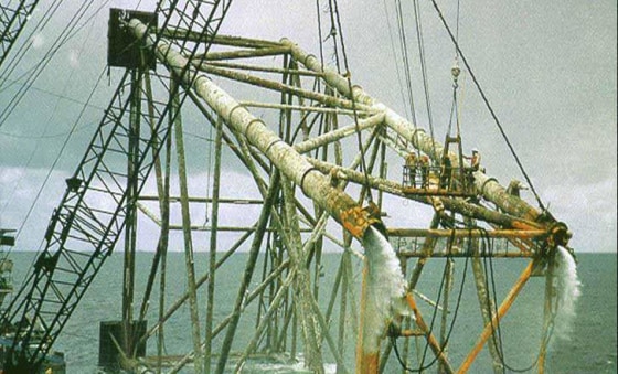 A platform "jacket" from a decomissioned well is lifted out of the water. The structures are often mammoth in size — notice the workers at right.