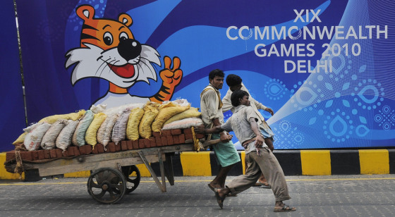 Image: Labourers pull a hand cart loaded with bricks and sacks of sand in front of boards advertising the 2010 Commonwealth Games in New Delhi