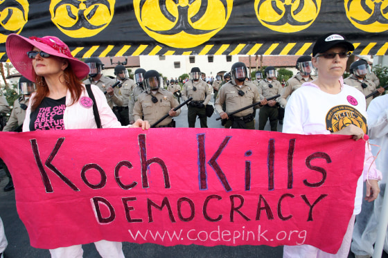 Image: Riverside County Sheriff's deputies in riot gear are seen behind Jodie Ivanes, of Venice Beach, Calif., left, and Ellen Sturtz, of West Los Angeles, right, during a protest dubbed the \"Koch Busters Rally\"