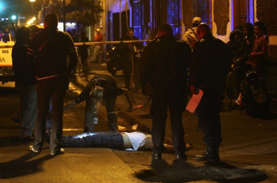 Image: A forensic worker takes measurements around the body of a dead man who was killed in a shootout in downtown Guadalajara