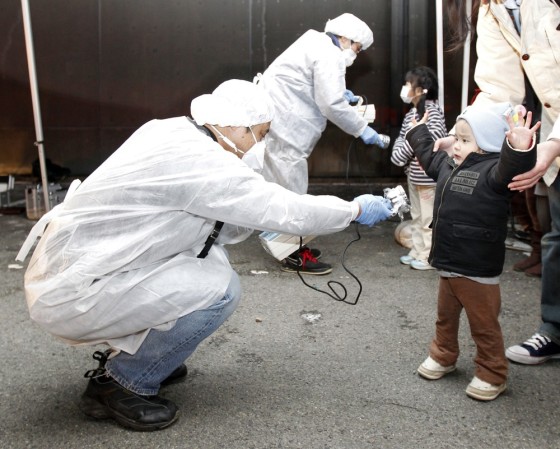 Image: Officials in protective gear check for signs of radiation on children who are from the evacuation area near the Fukushima Daini nuclear plant in Koriyama
