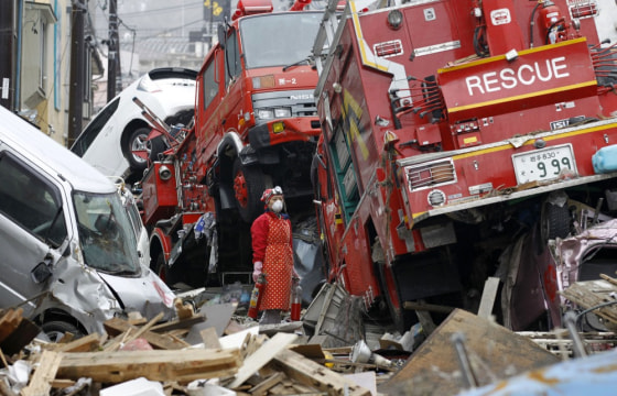 Image: Woman holds fire extinguishers as she cleans her house among the ruins of the destroyed residential part of Kamaishi