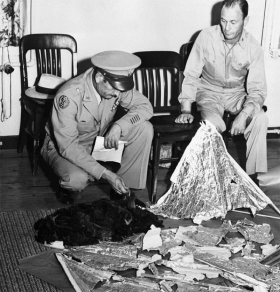 Brig. Gen. Roger M. Ramey, commanding general of 8th Air Force, and Col. Thomas J. Dubose, 8th Air Force chief of staff, identify metallic fragments found by a farmer near Roswell, N.M., as pieces of a weather balloon. This is the basis of the Roswell Incident, the supposed crash of an alien spacecraft.