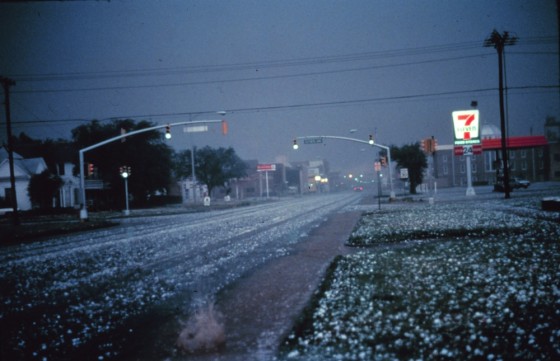 Large hail collects on streets and grass during a severe thunderstorm. Larger stones appear to be nearly 2 to 3 inches in diameter.