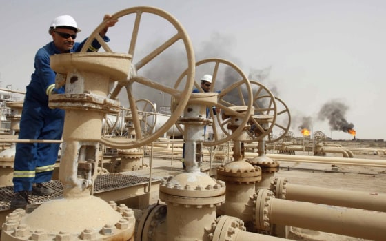 Image: Workers adjust the valves of an oil pipe as smoke rises from burning excess gas in Zubair oilfield in Basra