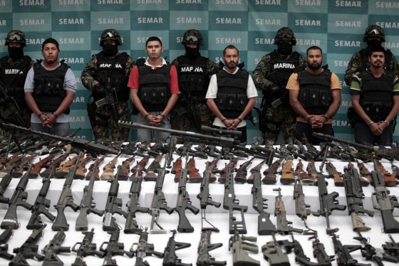 Image: Suspects are lined up as seized weapons are displayed to the media by the Mexican Navy in Mexico City