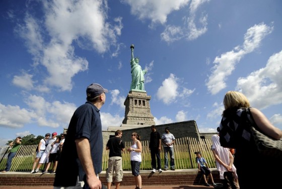 Image: Visitors pose for photographs in front of the Statue of Liberty in New York
