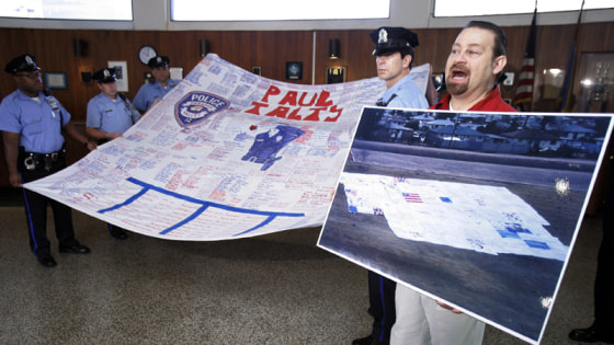 Image: n this Sept. 11, 2007 photo, American Quilt Memorial organizer Kevin Held holds up a photo of several quilts next to members of the Philadelphia Police Department
