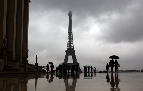 Image: Tourists protect themselves from the rain under umbrellas in front of the Eiffel tower in Paris as they visit the French capital during summer holidays