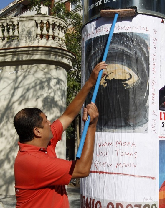 Image: A worker puts up a poster by Balearic artist Barcelo, painted for his bullfighter friend Tomas to mark the last bullfight in Catalonia, in Barcelona