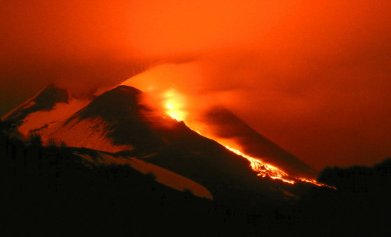 Italy's Mount Etna glows as lava pours down its flanks.