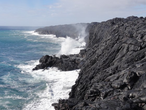 Lava from Kilauea volcano in Hawaii drops into the ocean. Steam plumes rise where the molten rock meets the sea.
