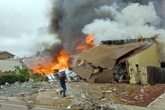 Man walks past burning debris after a military jet crashed into homes in San Diego