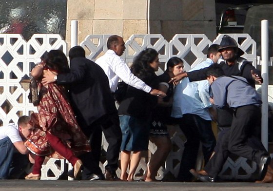People duck as gunshots are fired from inside the Taj Mahal hotel in Mumbai