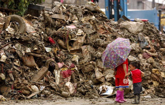 A mother and her child in Marikina, a Manila suburb, on Monday walk past debris left by two earlier storms in the Philippines. 