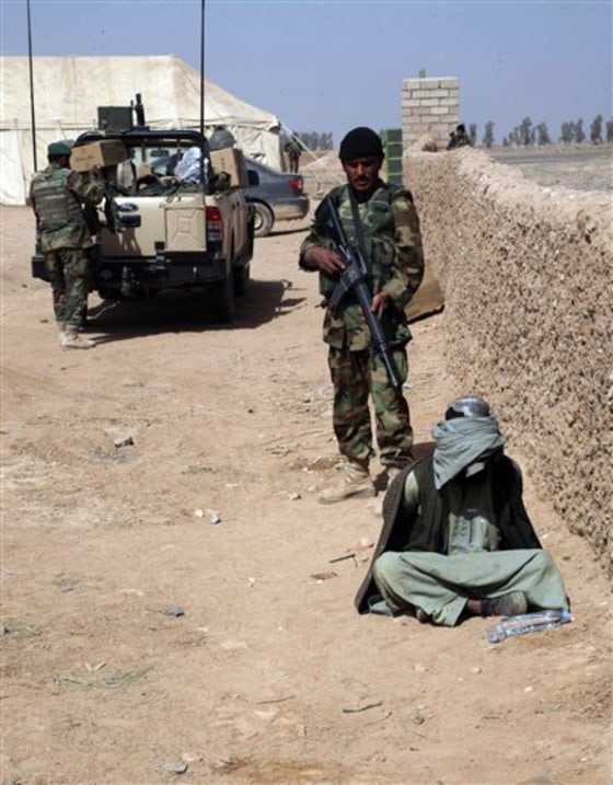 An Afghan National Army (ANA) soldier stands guard as a suspected Taliban sits blindfolded and hands tied on the ground in Marjah, city of Helmand province, Feb. 18.