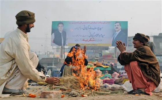 Backdropped by a billboard showing Pakistani Prime Minister Yousuf Raza Gilani, right, and his son Abdul Qadir, vendors gather around a fire to warm themselves, in Multan, Pakistan, Thursday, Jan. 6, 2010. Pakistan's prime minister says his government will reverse unpopular fuel price hikes that helped spark the break-up of the governing coalition. (AP Photo/Khalid Tanveer)
