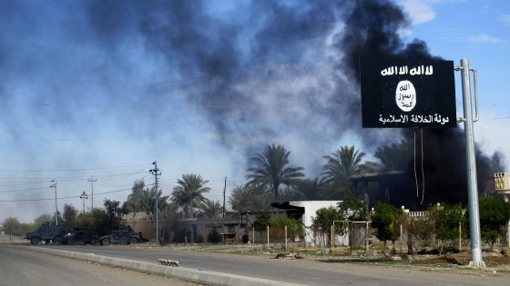 Smoke raises behind an Islamic State flag after Iraqi security forces and Shiite fighters took control of Saadiya in Diyala province from Islamist State militants, Nov. 24, 2014. (Photo by Stringer/Reuters)