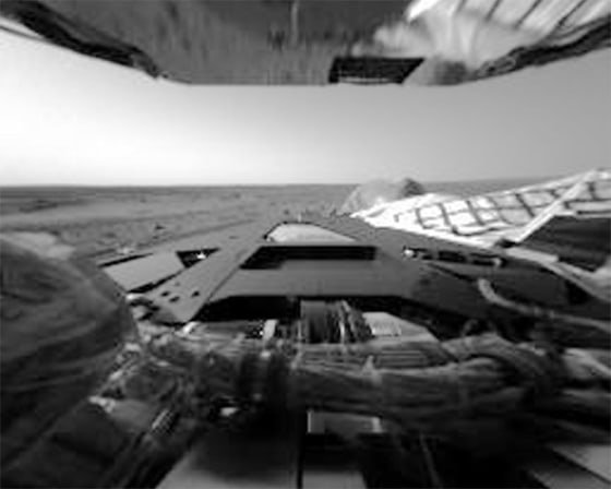 This image shows the rover's rear lander petal with a reflection from the bottom of a solar array at the top of the image. The Martian horizon and sky are visible in the background.