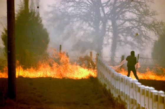 A volunteer uses a bucket to try to douse a grass fire south of Duncan, Okla., Wednesday.